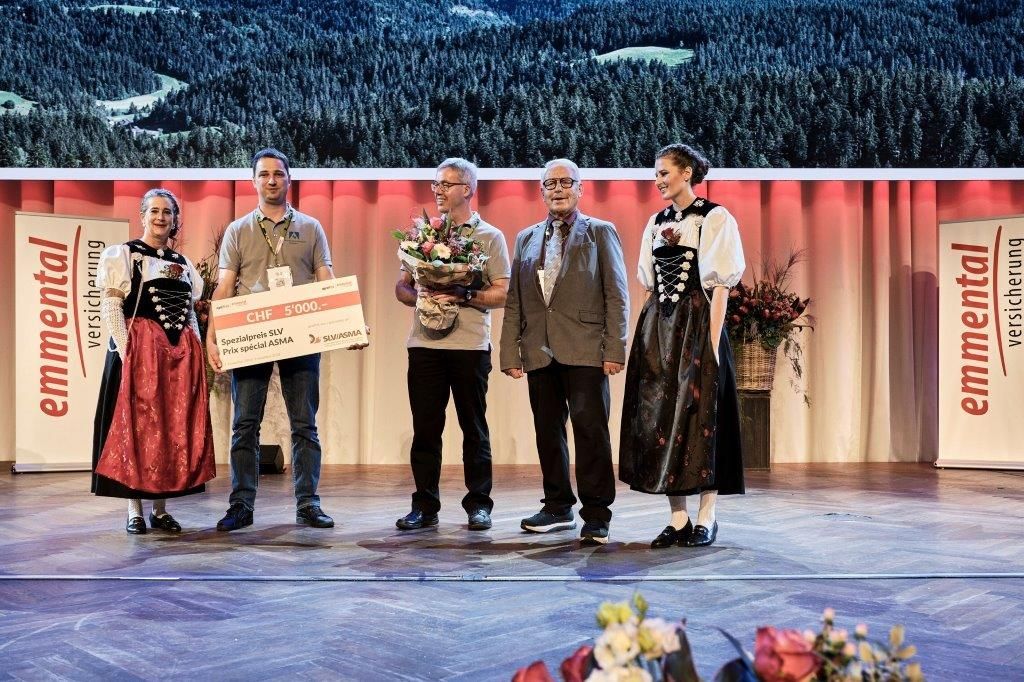 Stefan Isaak, Landmaschinenmechaniker und Maschinenbautechniker HF (2. v. li.), und Markus Ryser, Geschäftsinhaber (3. v. li.), auf der Bühne im Berner Kursaal. Bendicht Hauswirth vom SLV (2. v. r.) überreicht die Auszeichnung und den symbolischen Scheck über 5'000 CHF.