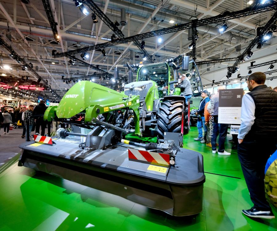 Messebesucher bestaunen einen modernen Fendt-Traktor mit Frontmähwerk an der Agritechnica.